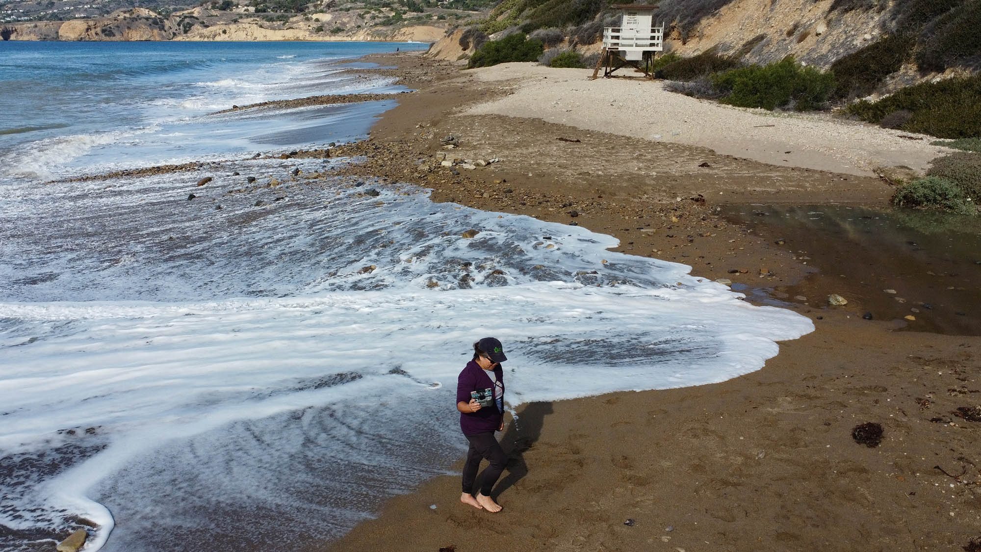 Myrna Aguilar walks on beach while holding Drone controller