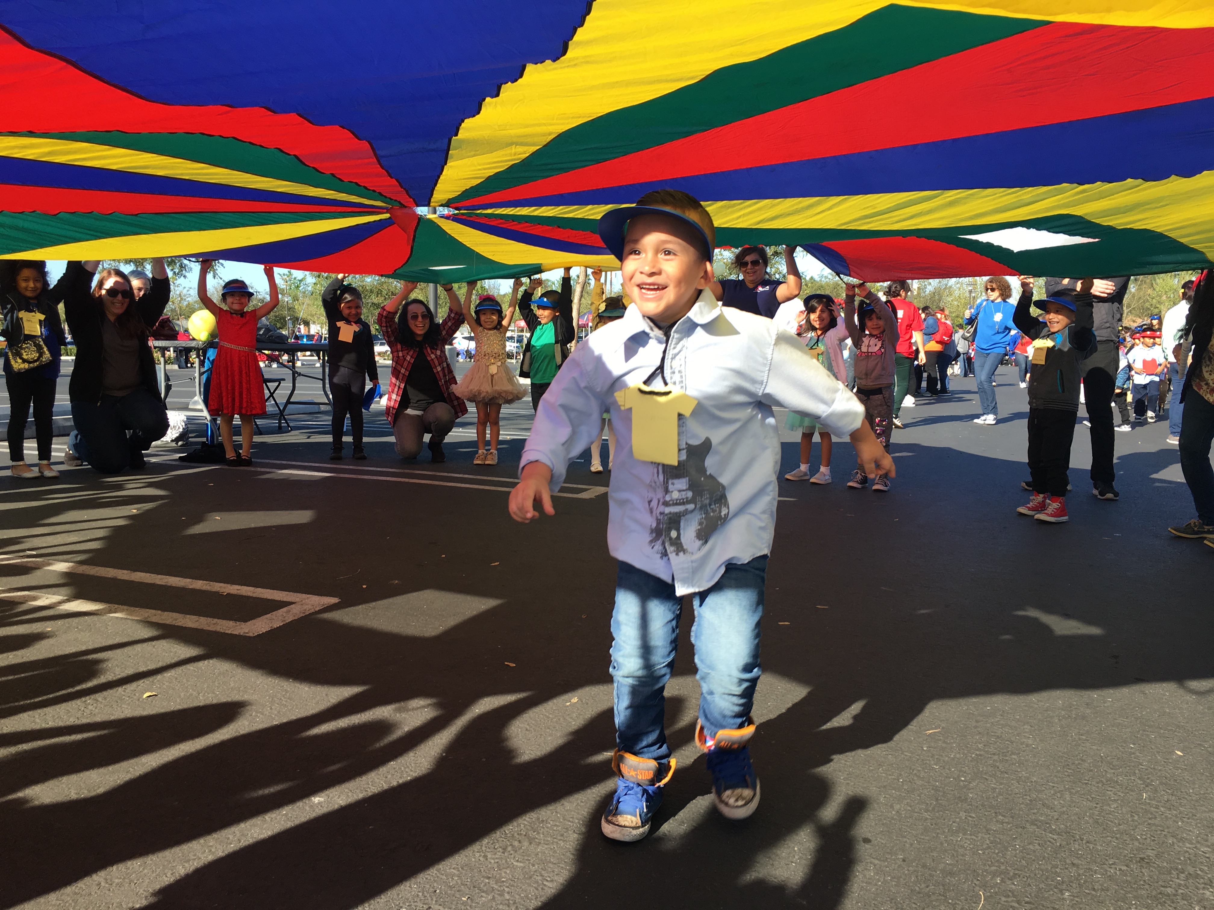 A kindergartener running under a giant parachute