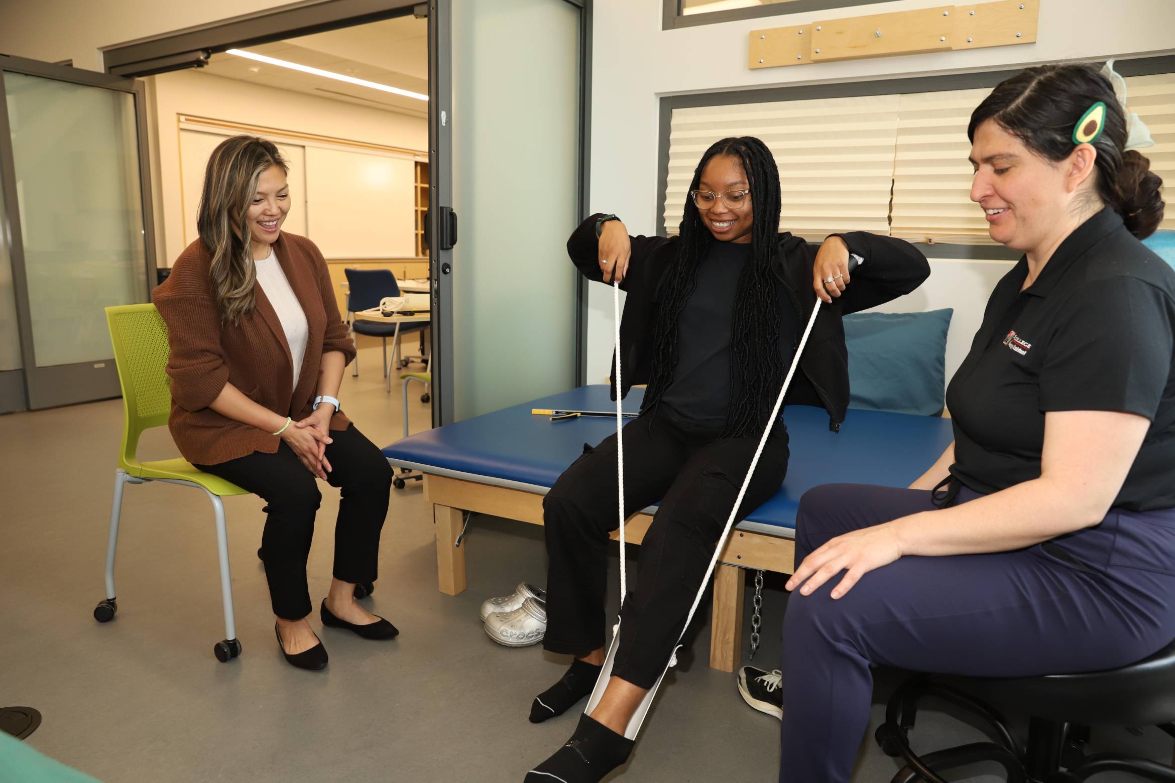 an occupational studies female student learning how to put on shoes in front of her classmate and instructor