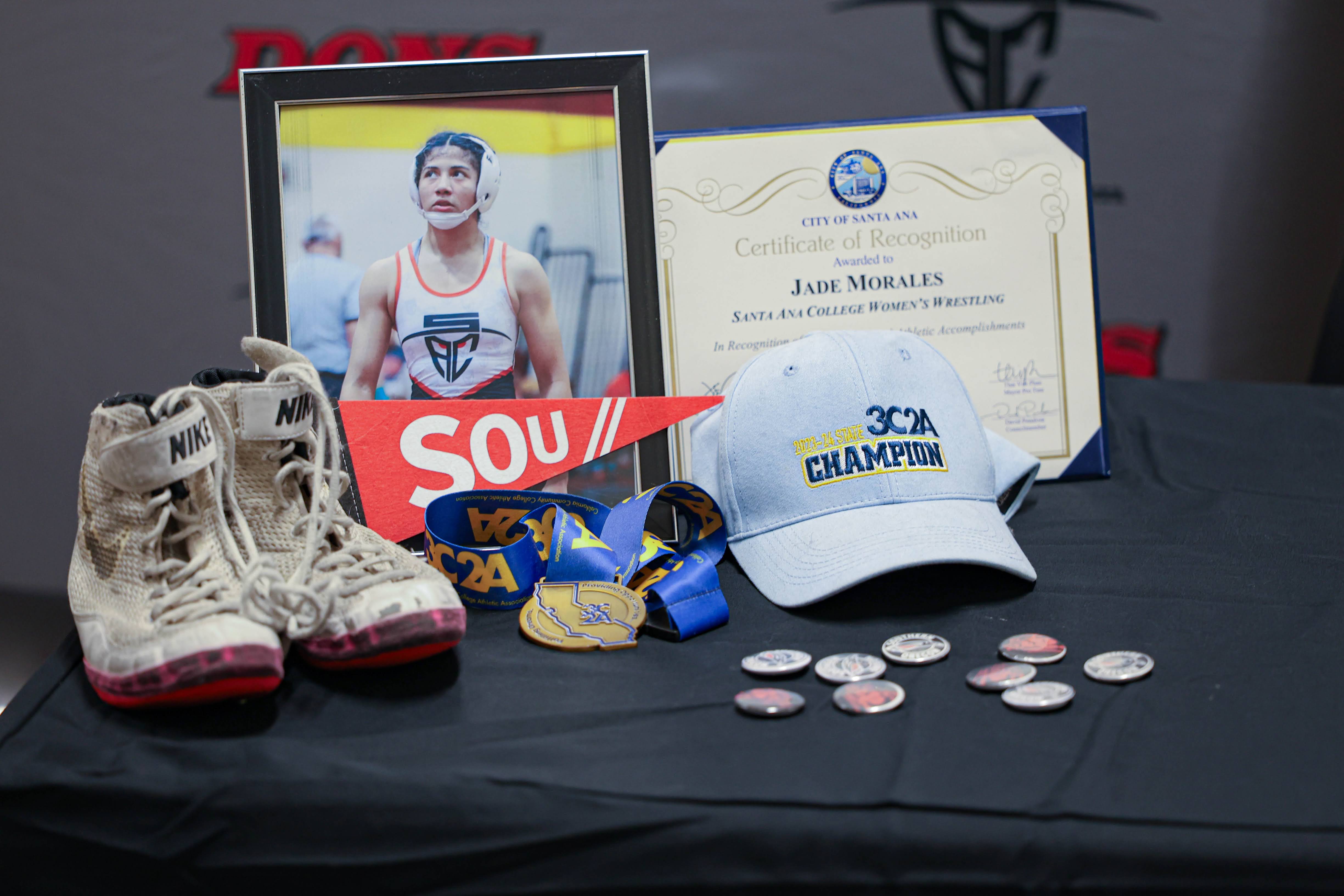 Jade's certificate of recognition by Santa Ana, gold medal from the state championship, wrestling shoes, and portrait on display