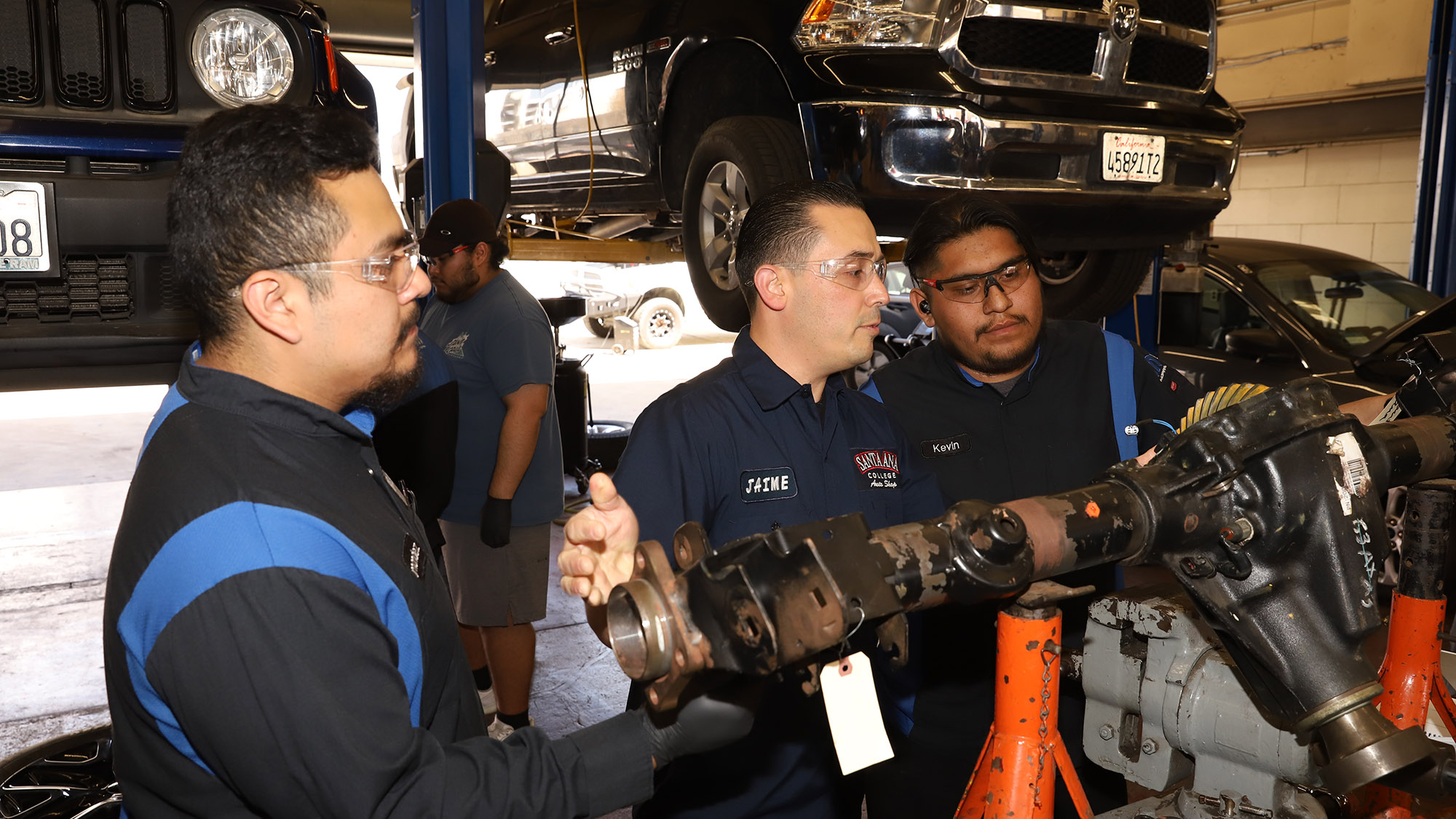 two auto tech students learn in the practice shop from an instructor