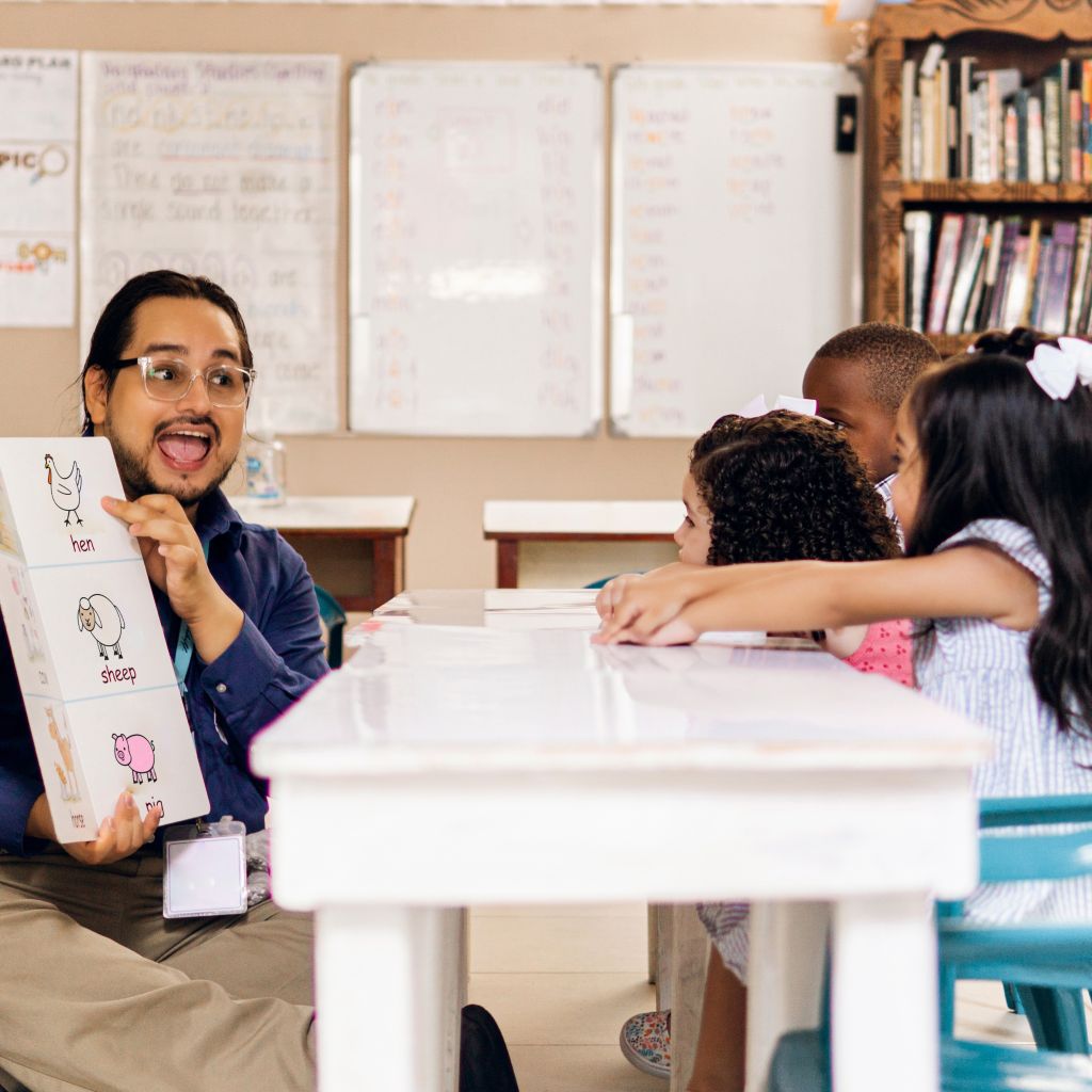 Excited latino man teaching young kids in early childhood education school