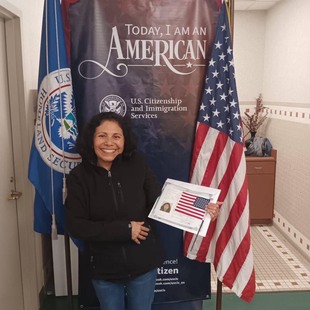 Smiling Latina woman holding American flag and certificate of naturalization after passing Citizenship test with help from teachers at Santa Ana College.