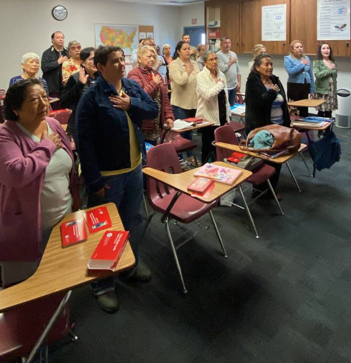 Citizenship students giving the pledge of allegiance to the United States flag in preparation for becoming American citizens.