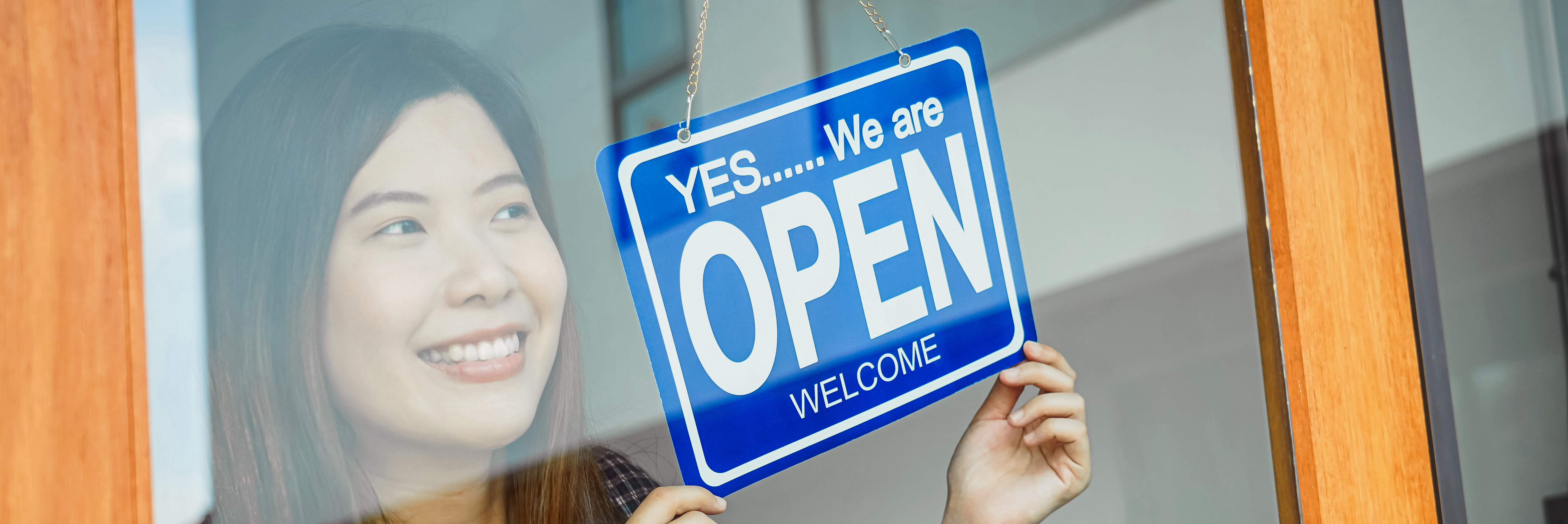 Woman holding OPEN sign in front of store