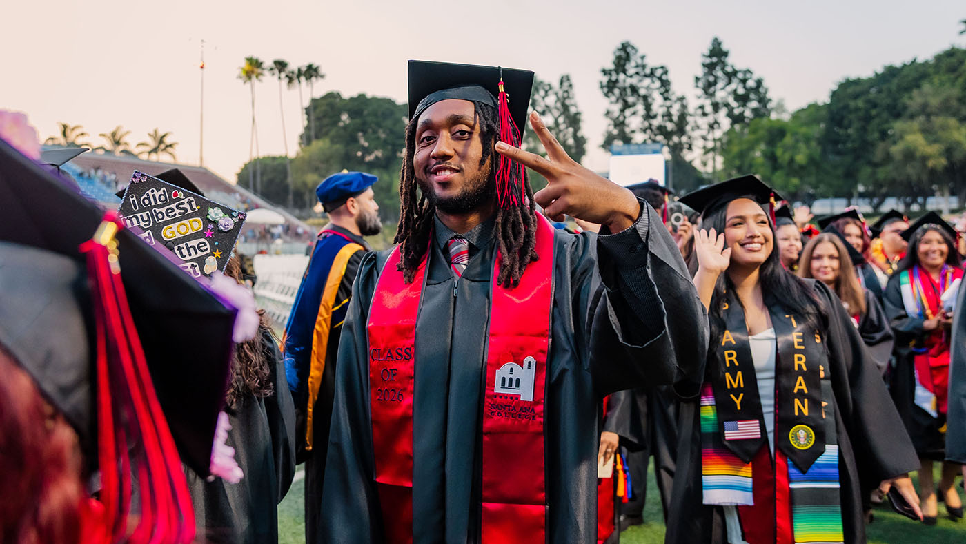 Black male student in graduation outfit holding up peace sign
