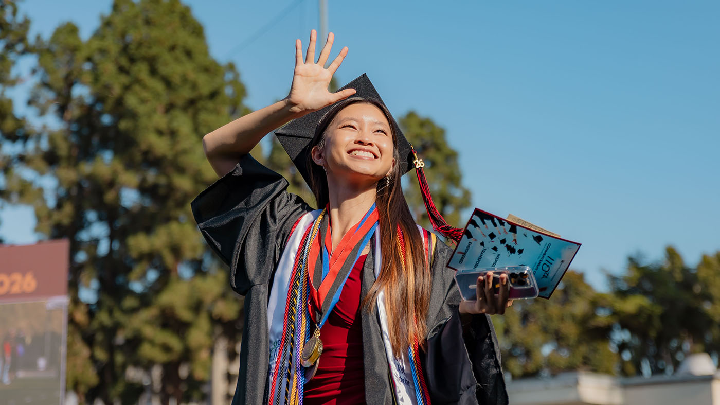 Asian female student waving while in graduation outfit