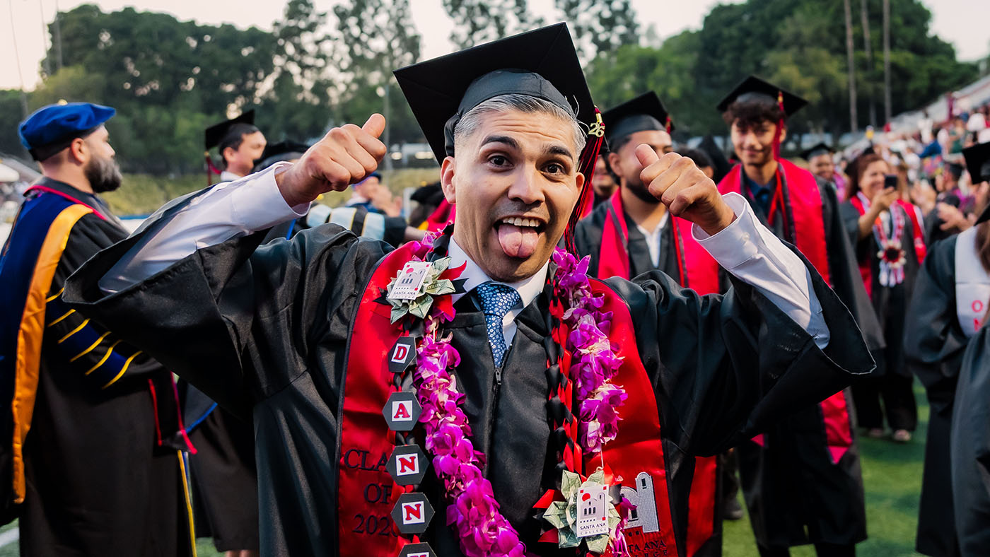 Male latino student in graduation outfit flexing in front of camera